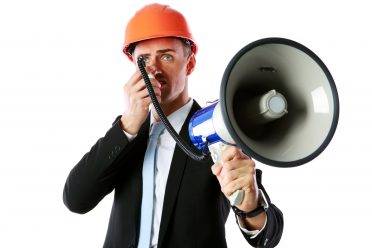 Businessman in helmet shouting with megaphone over white background