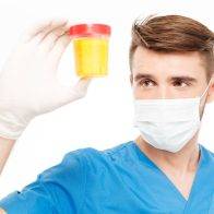 Male surgeon with mask holding bottle of urine sample isolated on white background