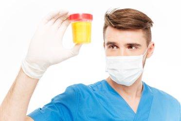 Male surgeon with mask holding bottle of urine sample isolated on white background