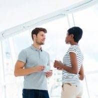Two young business people standing and talking in office during coffee break