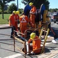 Group of construction workers running a pipe into a confined space in the middle of the road.