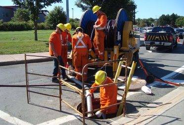 Group of construction workers running a pipe into a confined space in the middle of the road.