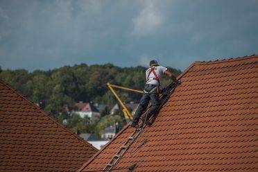 Worker on top of a roof installing shingles.