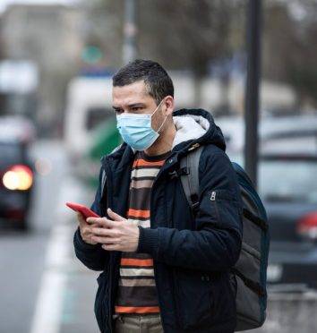 Coronavirus protection. Mature man in the city after the work day, wearing protective mask on the face. Calling for a taxi.