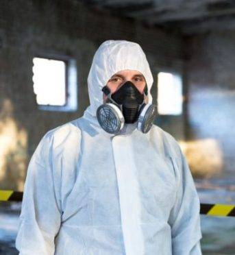 A man is dressed in a chemical protective overalls and a half mask with air filters and safety glasses.