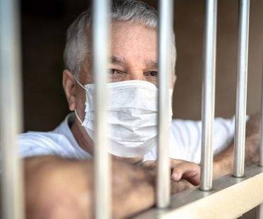 Man wearing a mask behind bars.